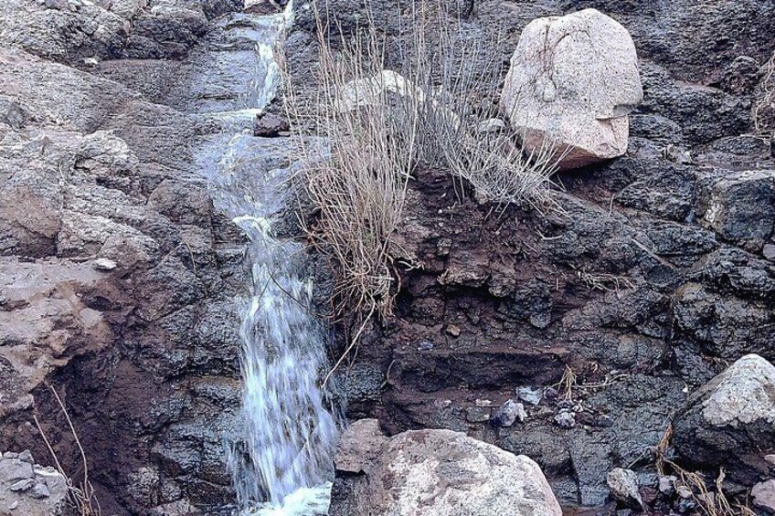 Un torrente roccioso con acqua corrente, circondato da erba secca e grosse rocce. 3