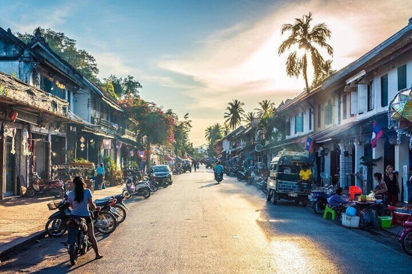 A street lined with traditional buildings, motorcycles parked along the sides, and a tuk-tuk in the distance. 2