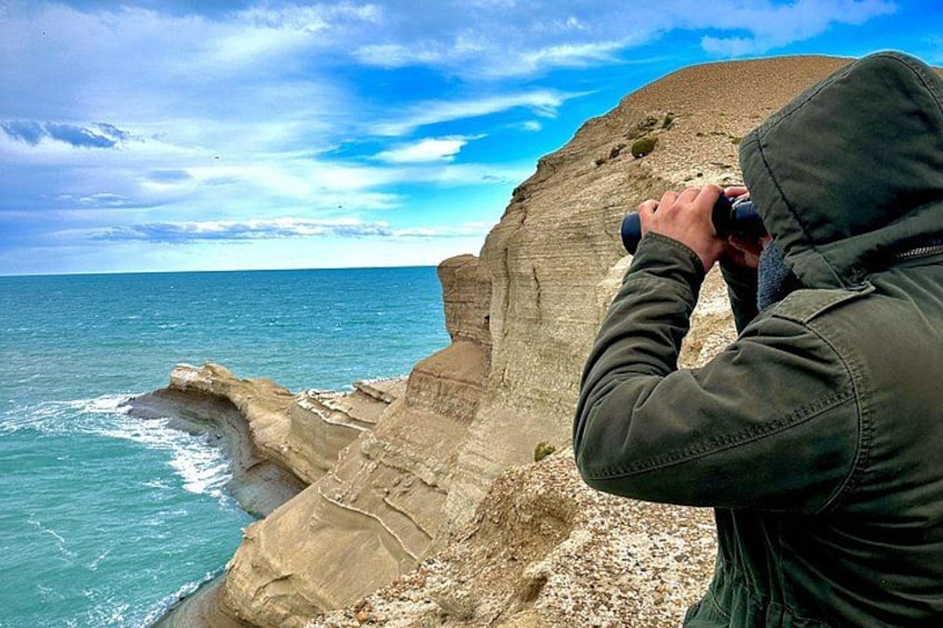 A person taking a photograph of a coastal cliff with the ocean in the background. 5