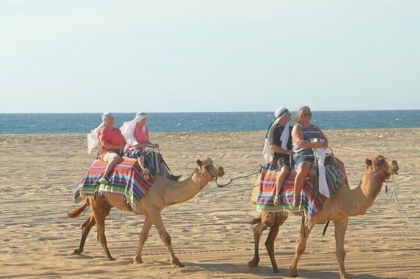 Een kameelkaravaan op een zanderig strand met mensen die op kamelen rijden. 2