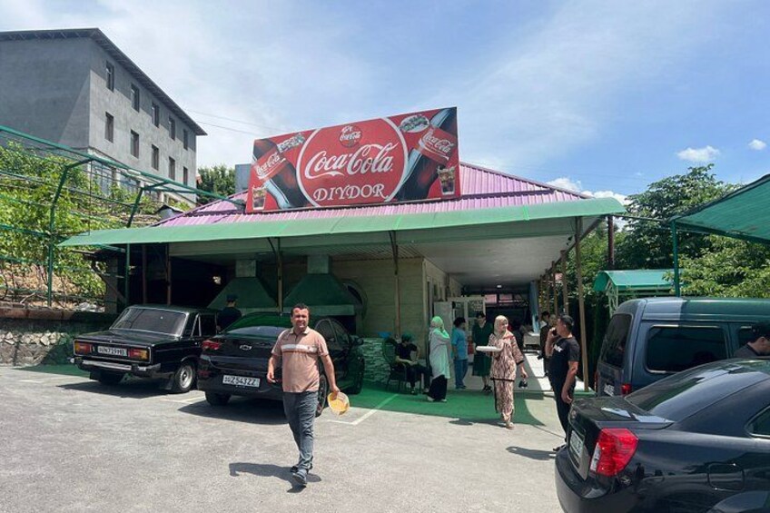 A Coca-Cola branded outdoor dining area with a covered roof, a parked car, and a person walking. 4
