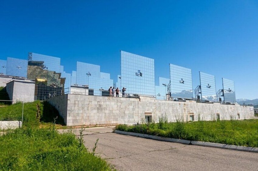 A solar farm with large reflective panels, a concrete structure, and a clear blue sky. 5