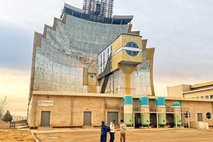 A large industrial building with a unique, angular design, featuring a glass facade and multiple green cylindrical structures at its base. 3