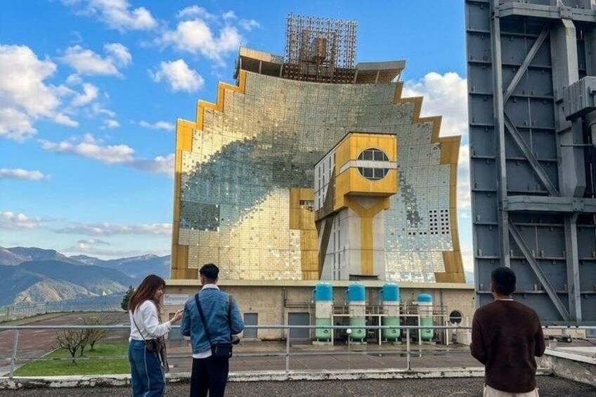 A large, uniquely designed building with a geometric facade, a staircase, and a view of mountains in the background. 1
