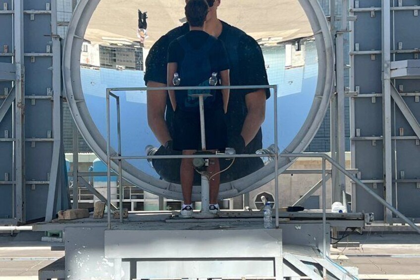 A person standing on a platform with a large circular structure behind them. 2