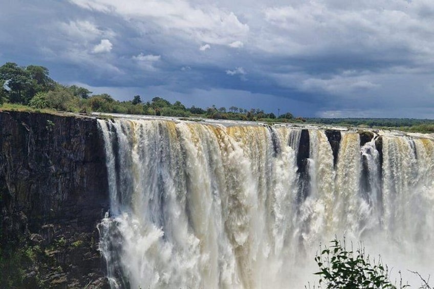 A large waterfall with multiple cascades, surrounded by lush greenery and a cloudy sky. 4