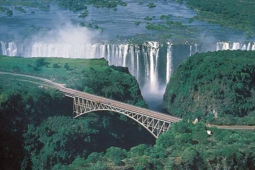 A bridge over a waterfall with lush greenery around. 1