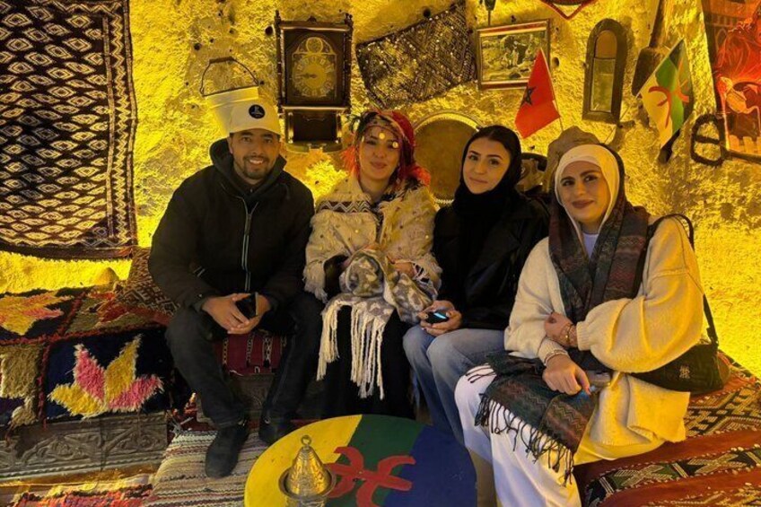 Un gruppo di persone sedute su una panchina decorata con tappeti tradizionali e un muro ornato da bandiere e opere d'arte. 2