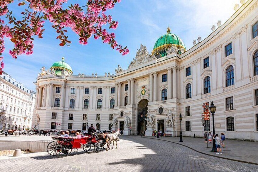 A historic building with ornate architecture, a green dome, and a cobblestone street with a horse-drawn carriage. 2