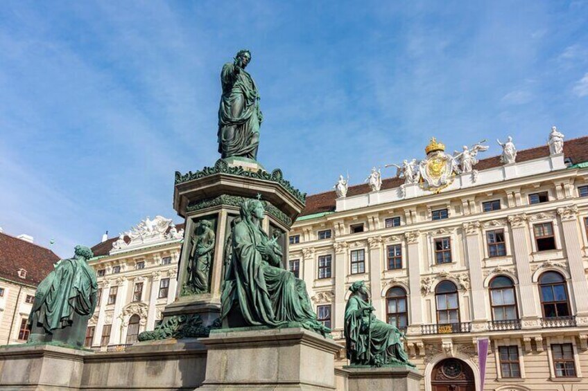 A statue of a woman in a dress, surrounded by other statues, in front of a large ornate building. 5