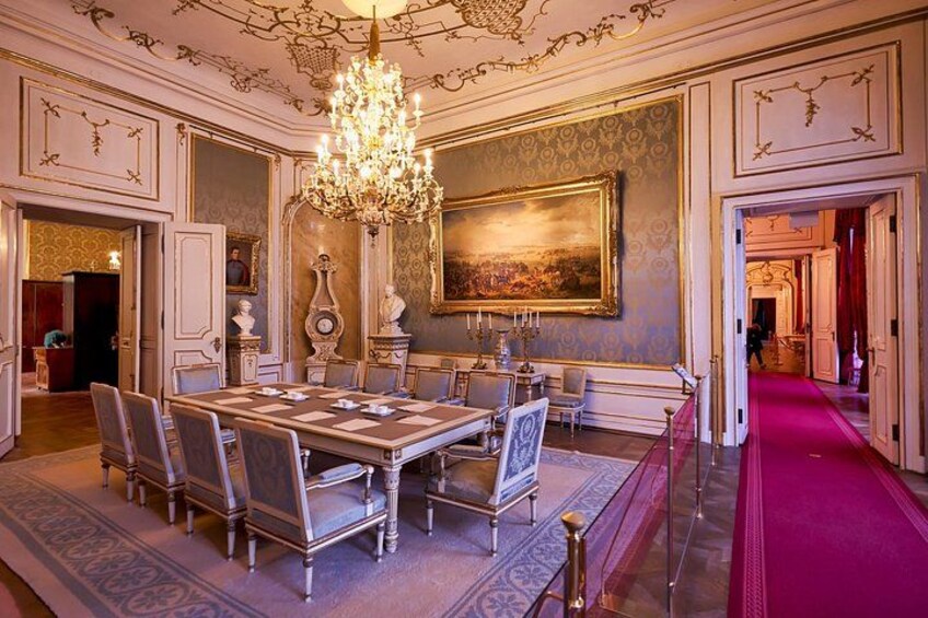 Een weelderige eetzaal met een grote kroonluchter, versierde wanddecoraties en een rood tapijt. 4