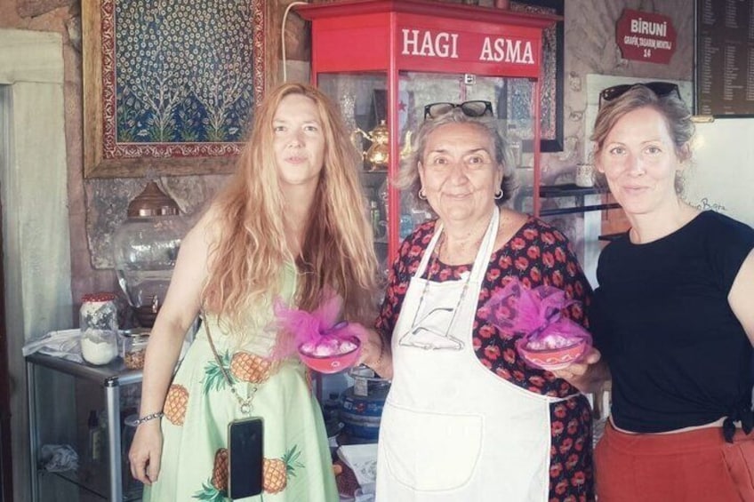 Trois personnes se trouvent dans une cuisine. On y voit un panneau rouge sur lequel est écrit « HAGI ASMA » et une peinture décorative sur le mur. 3