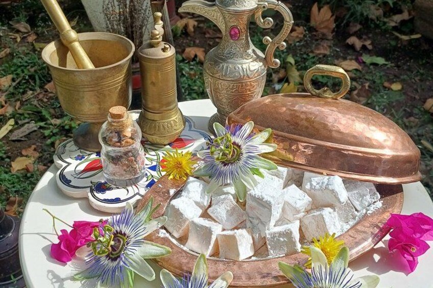 Una mesa con una olla de cobre, un mortero de latón, un frasco de especias y un plato con comida y flores. 1