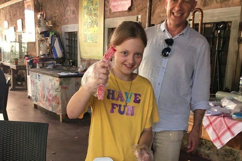 Una persona sosteniendo un objeto rojo, usando una camiseta amarilla con el texto 'HAVE FUN', de pie en un entorno exterior con un mostrador y varios artículos al fondo. 4