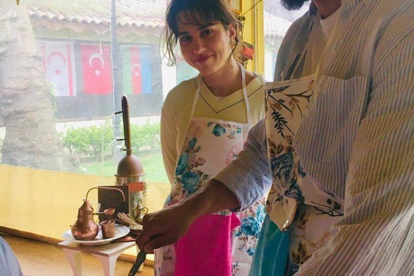 Una persona en una cocina con una olla de cobre sobre una estufa, una ventana con vista a un edificio y una mesa con mantel rosa. 3