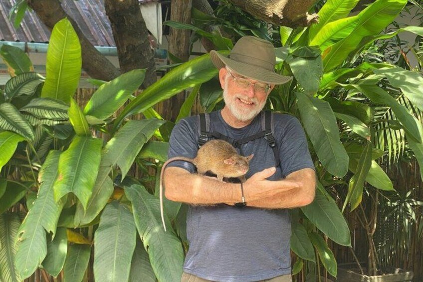 A man holding a small animal, surrounded by lush green foliage. 1