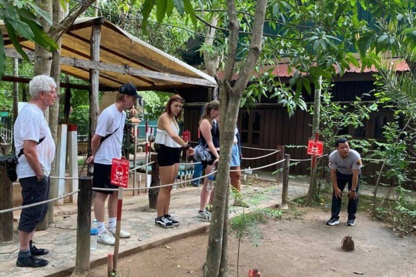 A group of people standing on a dirt path with trees and a wooden structure in the background. 4