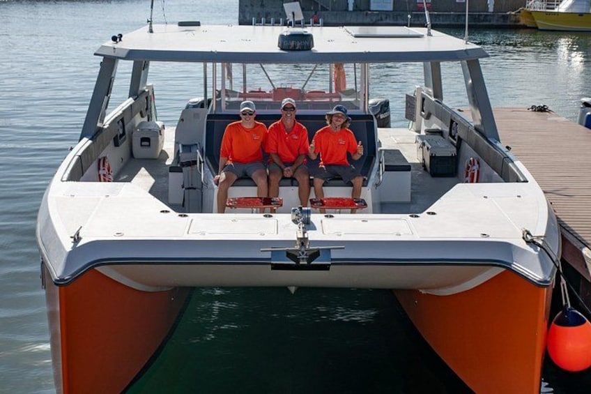 A boat with two people wearing orange life jackets, docked at a pier. 2