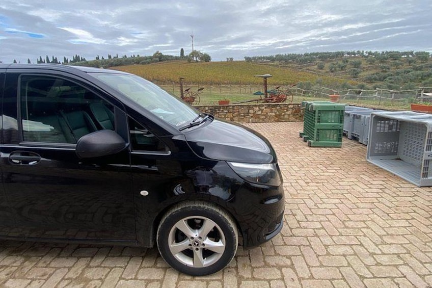 A black car parked on a paved area with a vineyard and rolling hills in the background. 2