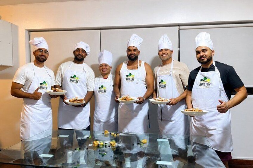 Five chefs in white aprons and hats holding plates of food. 3