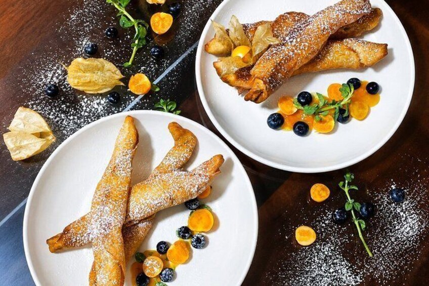 Three plates of fried pastries dusted with powdered sugar, accompanied by blueberries and apricots. 5