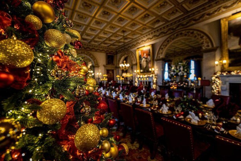 A grand hall with a decorated Christmas tree, ornate ceiling, and formal dining setup. 2