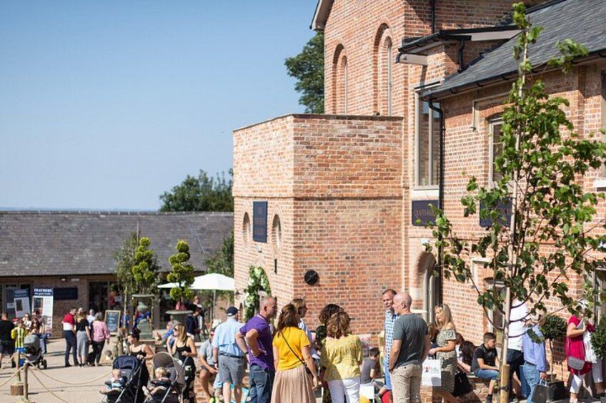A brick building with arched windows and a tower, surrounded by people and trees. 5