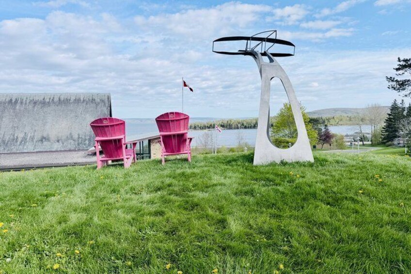 Un espace verdoyant agrémenté d’une sculpture moderne, de deux fauteuils Adirondack rouges et, au fond, d’une étendue d’eau. 3