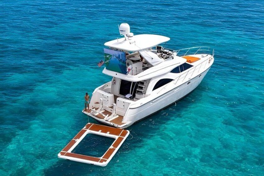 A white yacht with a covered deck and a small boat attached, floating in clear turquoise water. 1