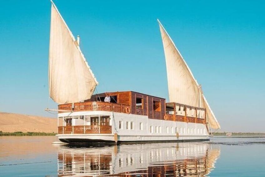 A large, traditional sailing boat with two large sails, wooden deck, and multiple windows, floating on calm water. 3