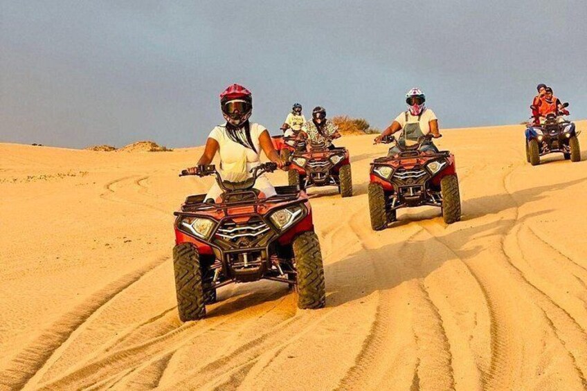 Four people riding ATVs on a sandy dune. 4