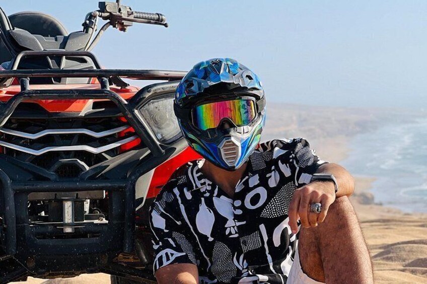 A person sitting on a dune with a quad bike. 3