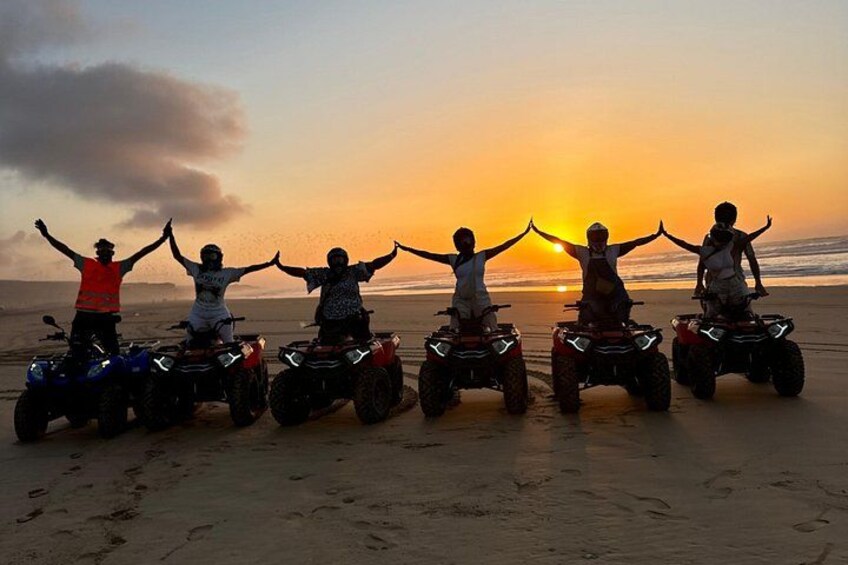 Five people on ATVs on a beach at sunset. 3