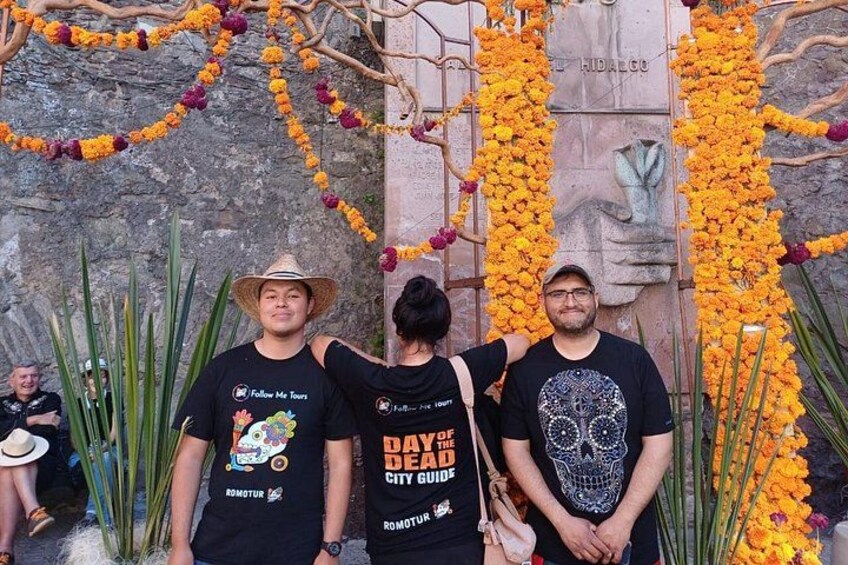 Three people standing in front of a stone monument with floral decorations. 2