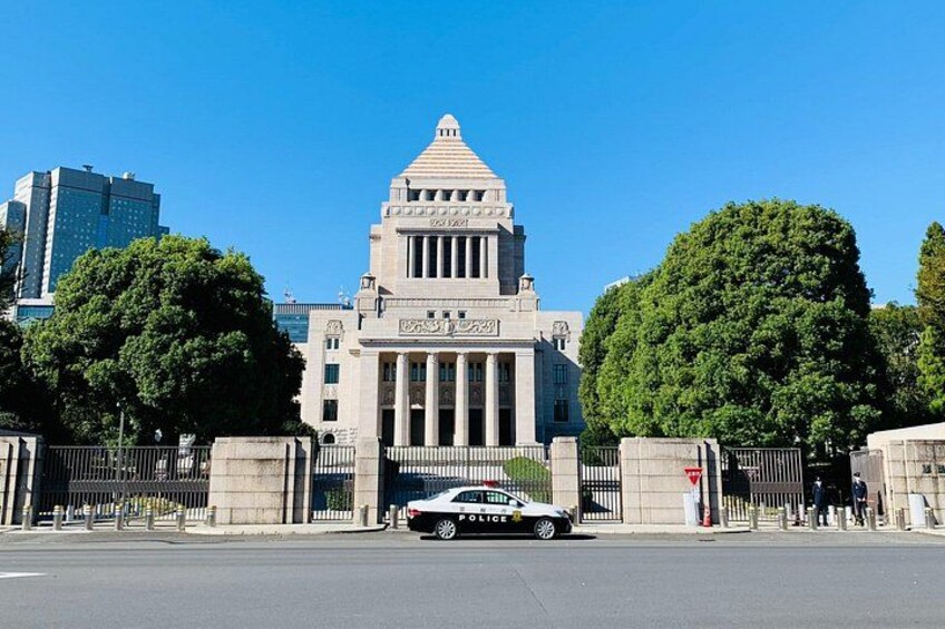 A large government building with a triangular roof and columns, surrounded by trees and a police car in front. 2