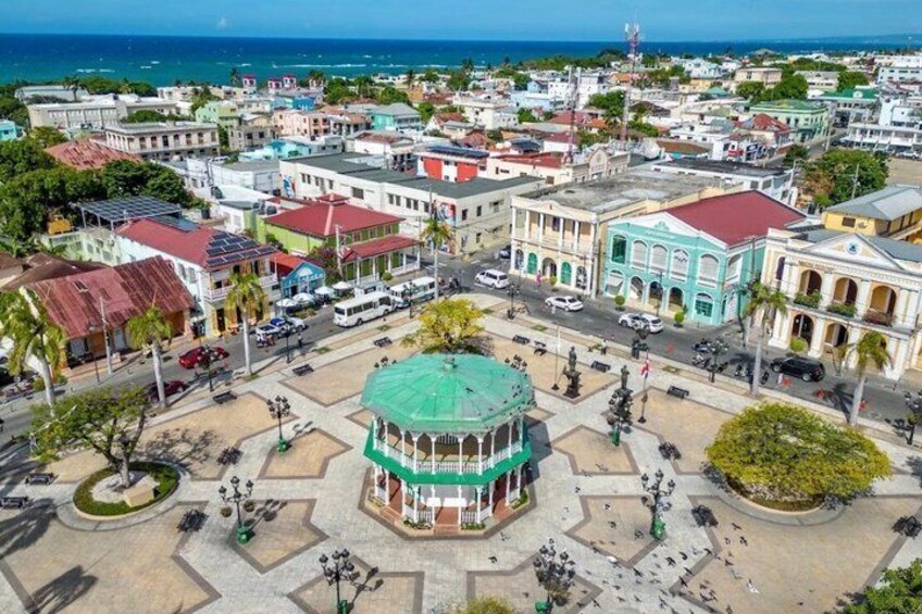 A town square with a central gazebo, surrounding buildings, and a view of the ocean. 3