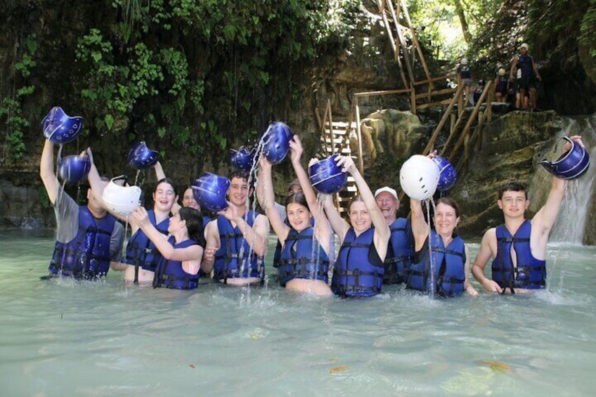 Un groupe de personnes vêtues de gilets de sauvetage bleus célèbre dans une étendue d’eau, avec une cascade en arrière-plan. 1