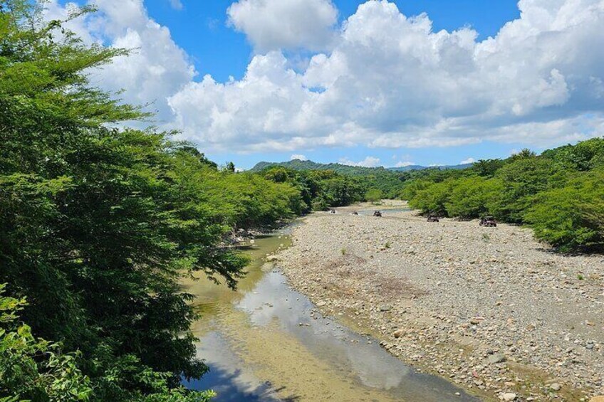 Une rivière au lit rocheux, bordée d’une végétation luxuriante et avec des collines en arrière-plan. 2