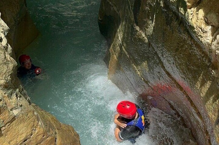 Une personne vêtue d’une veste bleue et d’un casque rouge navigue dans un étroit canal d’eau bordé de parois rocheuses. 3