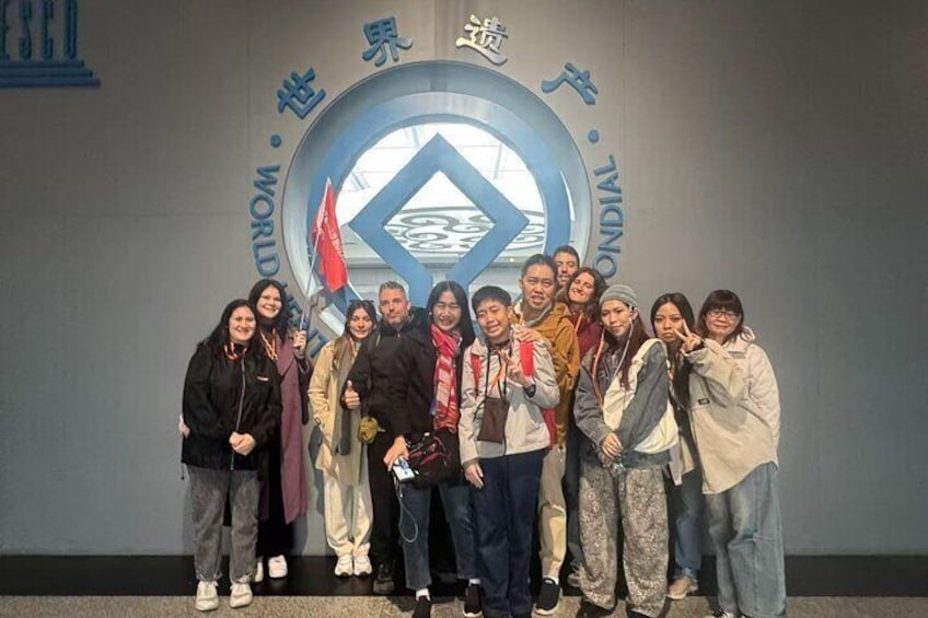 Un grupo de personas posando frente a un gran emblema circular con texto y una bandera. 3