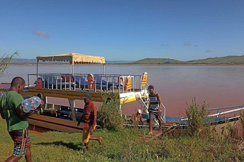 A group of people near a boat on a river with a canopy, some standing and some walking. 5