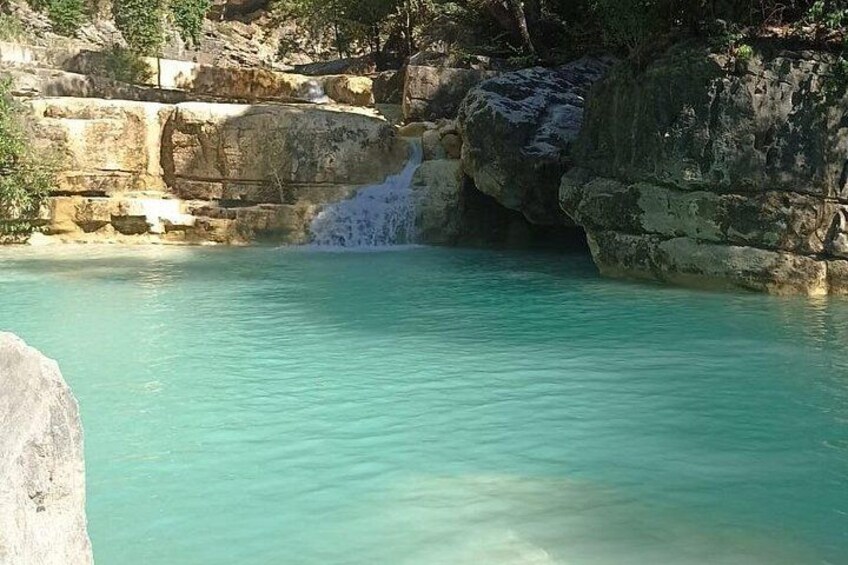 A turquoise pool with a waterfall, surrounded by rocky terrain. 3
