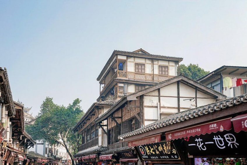 A traditional street with wooden buildings, a signboard, and a tree. 2