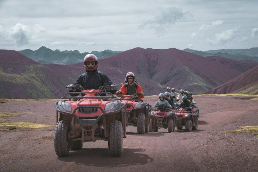 Un groupe de personnes circulant en quads sur un chemin de terre, avec des montagnes en arrière-plan. 3