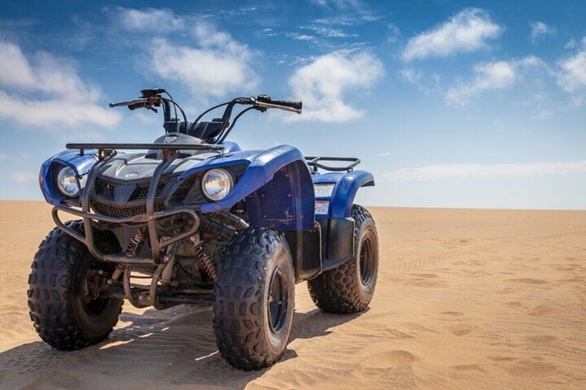 En blå quad bike i en ørken med sandklitter i baggrunden. 2