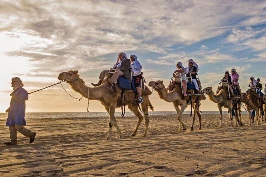 A group of people riding camels on a beach at sunset. 4