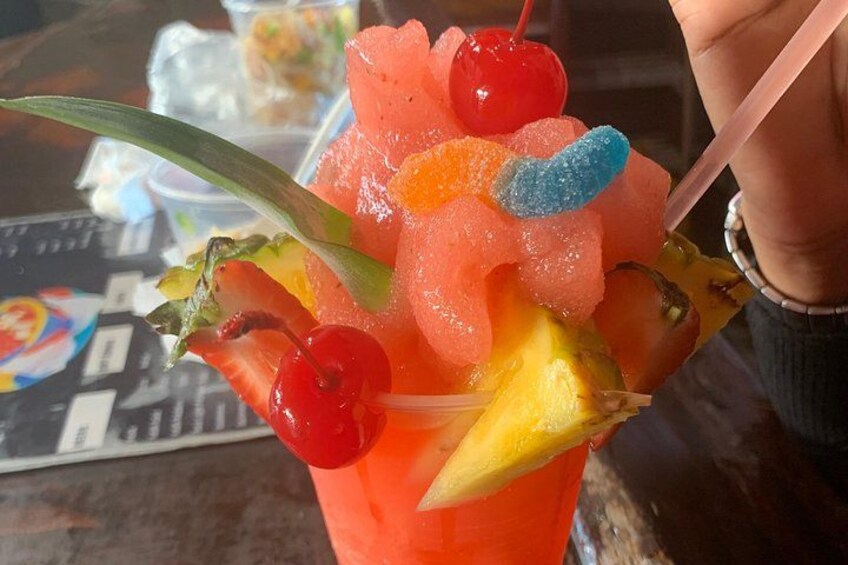 En färgglad cocktail med olika frukter och ett körsbär på glaskanten. 4