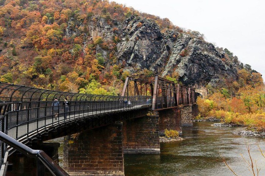 A metal bridge over a river with autumn foliage and a rocky hill in the background. 3