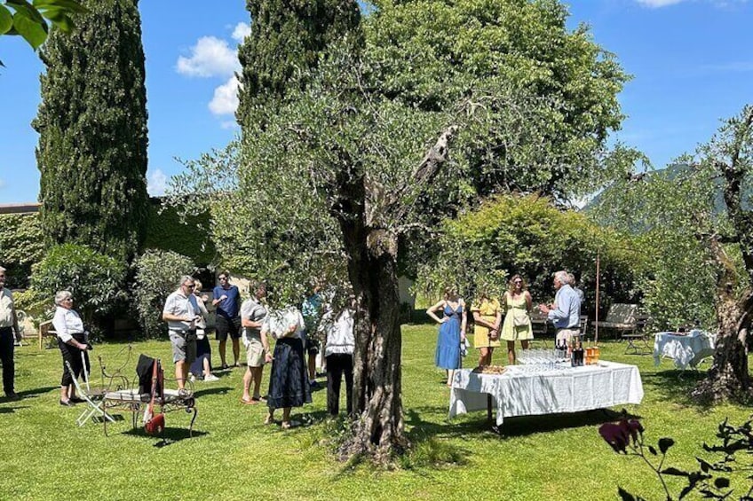 People gathered around a table in a grassy outdoor area with trees and a clear sky. 1