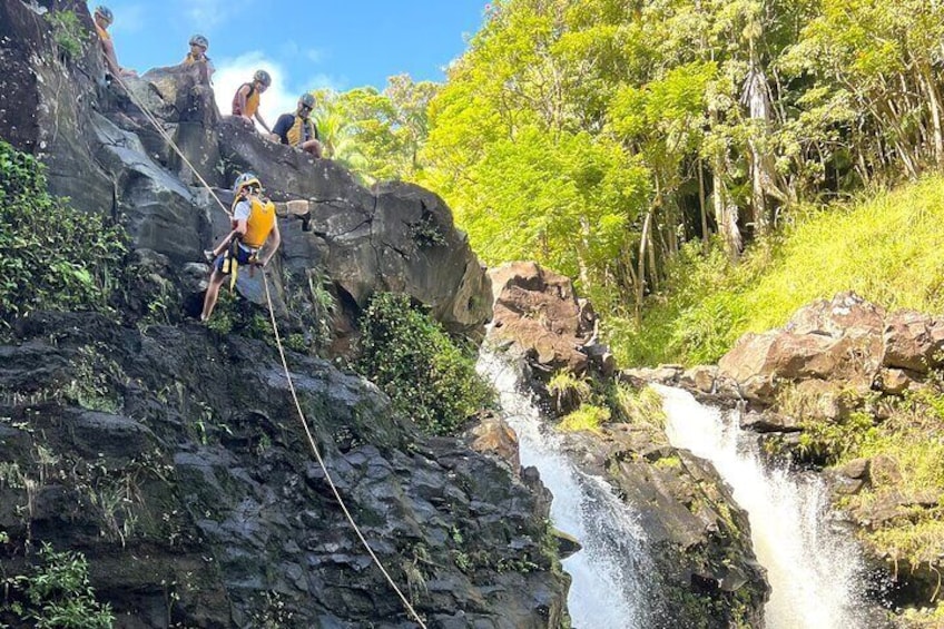 People rappelling down a rocky cliff with a waterfall in the background. 1